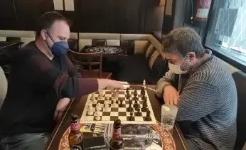 Dos socios con mascarilla juegan en un reservado del bar; uno de ellos mueve una pieza
